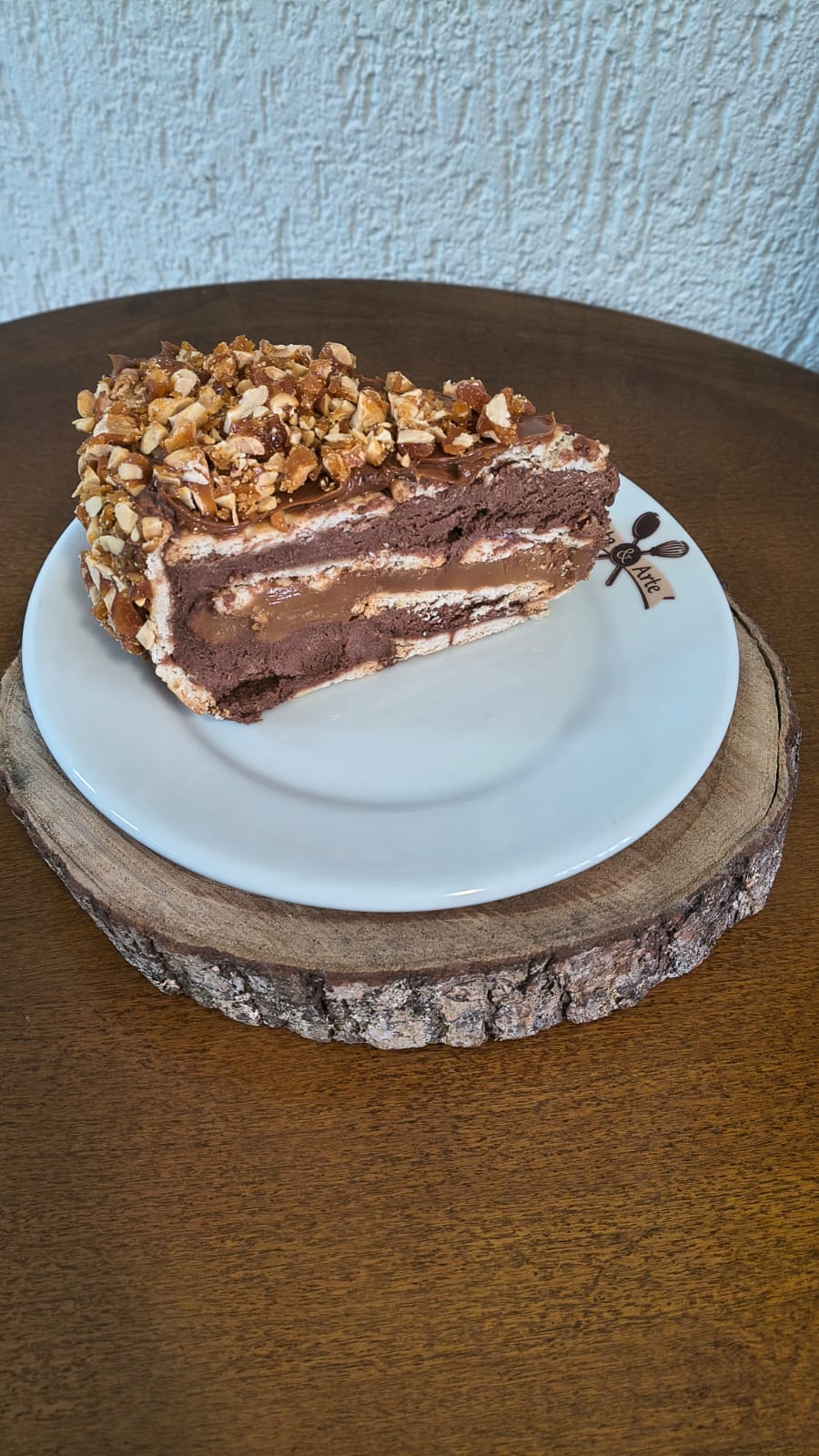 Fatia de torta de paçoca trufada, com camadas de creme e doce de leite, coberta com caramelo crocante e amendoim torrado